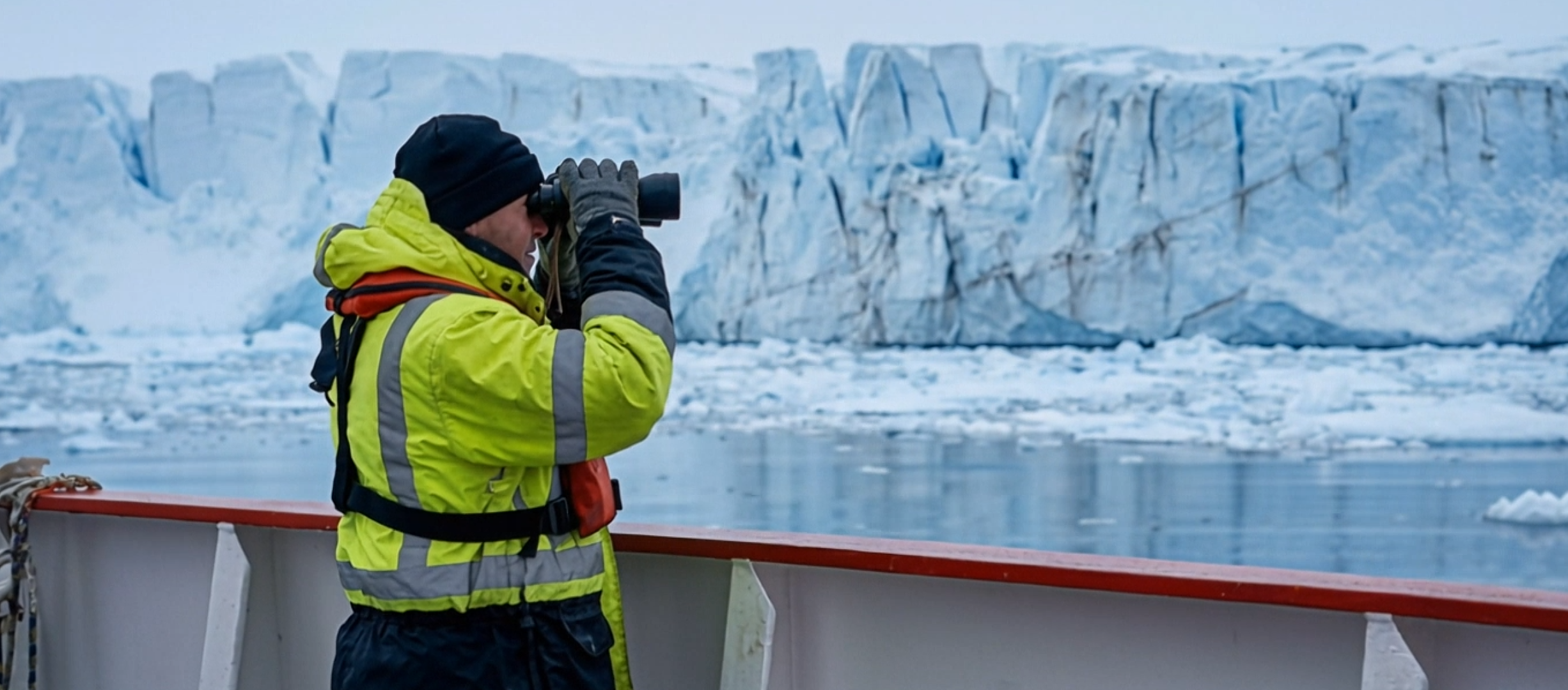 Crew member observing a glacier from the deck of a vessel