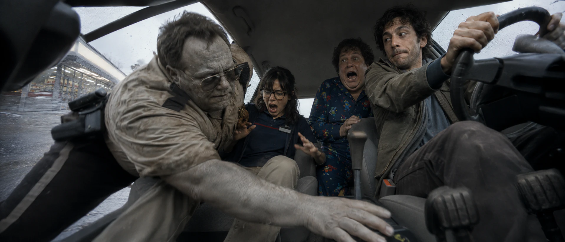 Low interior view of Leo driving while a zombie security officer reaches into the car
